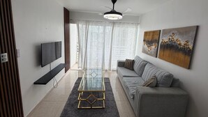 Uma sala de estar moderna com uma TV de tela plana, uma mesa de centro de vidro, um sofá cinza e obras de arte nas paredes.
