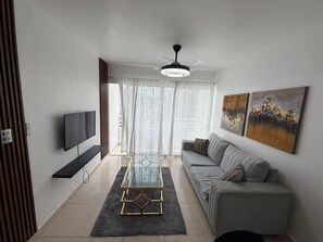 A modern living room with a flat-screen TV, a glass coffee table, a gray sofa, and artwork on the walls.