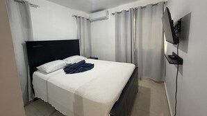 Quarto com cama, cortinas, televisão e ar condicionado.