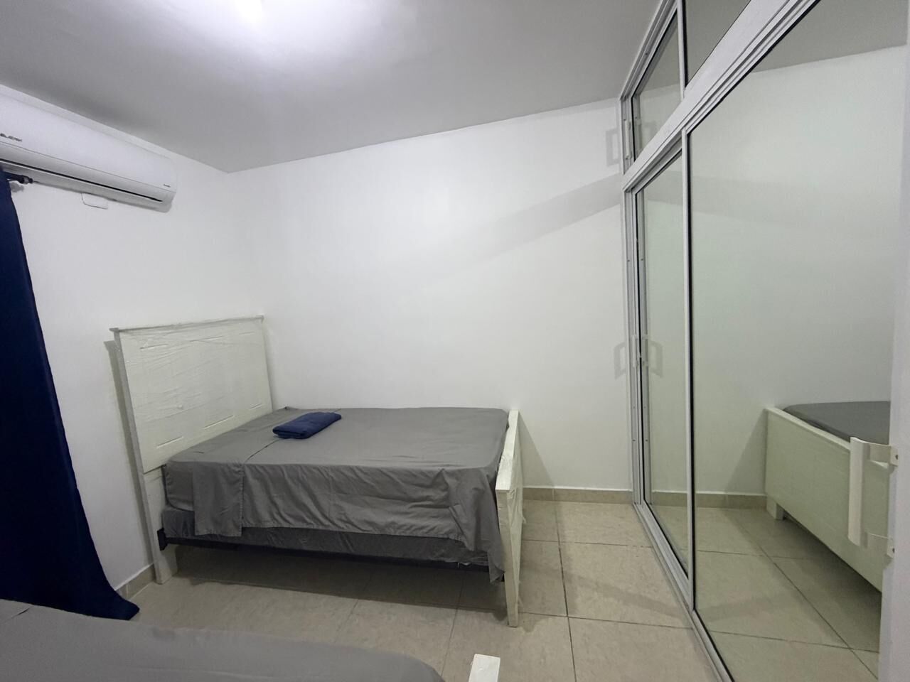 Ein kleines Zimmer mit einem Einzelbett, einem Schiebetürenschrank, weißen Wänden und einem gefliesten Boden.
