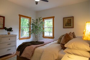 Une chambre à coucher avec un lit, une commode, une fenêtre avec une plante et un tableau au mur.