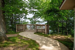 Eine Holzterrasse führt zu einem See, umgeben von Bäumen und einem Betonweg.