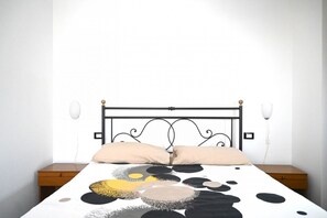 Un lit avec un cadre en métal noir, deux tables de chevet et une lampe fixée au mur.