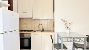A compact kitchen with a gas stove, oven, sink, and a dining area with a table and chairs. - SE265 – Senigallia, modern one-bedroom apartment with terrace and wi-fi (Senigallia)