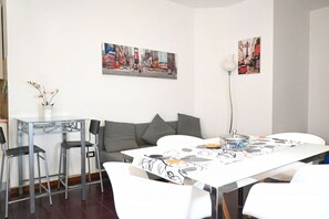 Un salon moderne comprenant un canapé, une table à manger avec des chaises, une table basse et deux tableaux accrochés au mur.