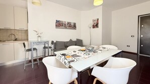 A modern dining area with a white table, two white chairs, a gray sofa, and a kitchen in the background. - SE265 – Senigallia, modern one-bedroom apartment with terrace and wi-fi (Senigallia)