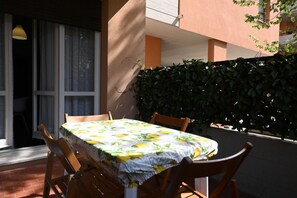 Un espace de restauration en plein air avec une table recouverte d’une nappe, entourée de chaises, et une haie en arrière-plan.