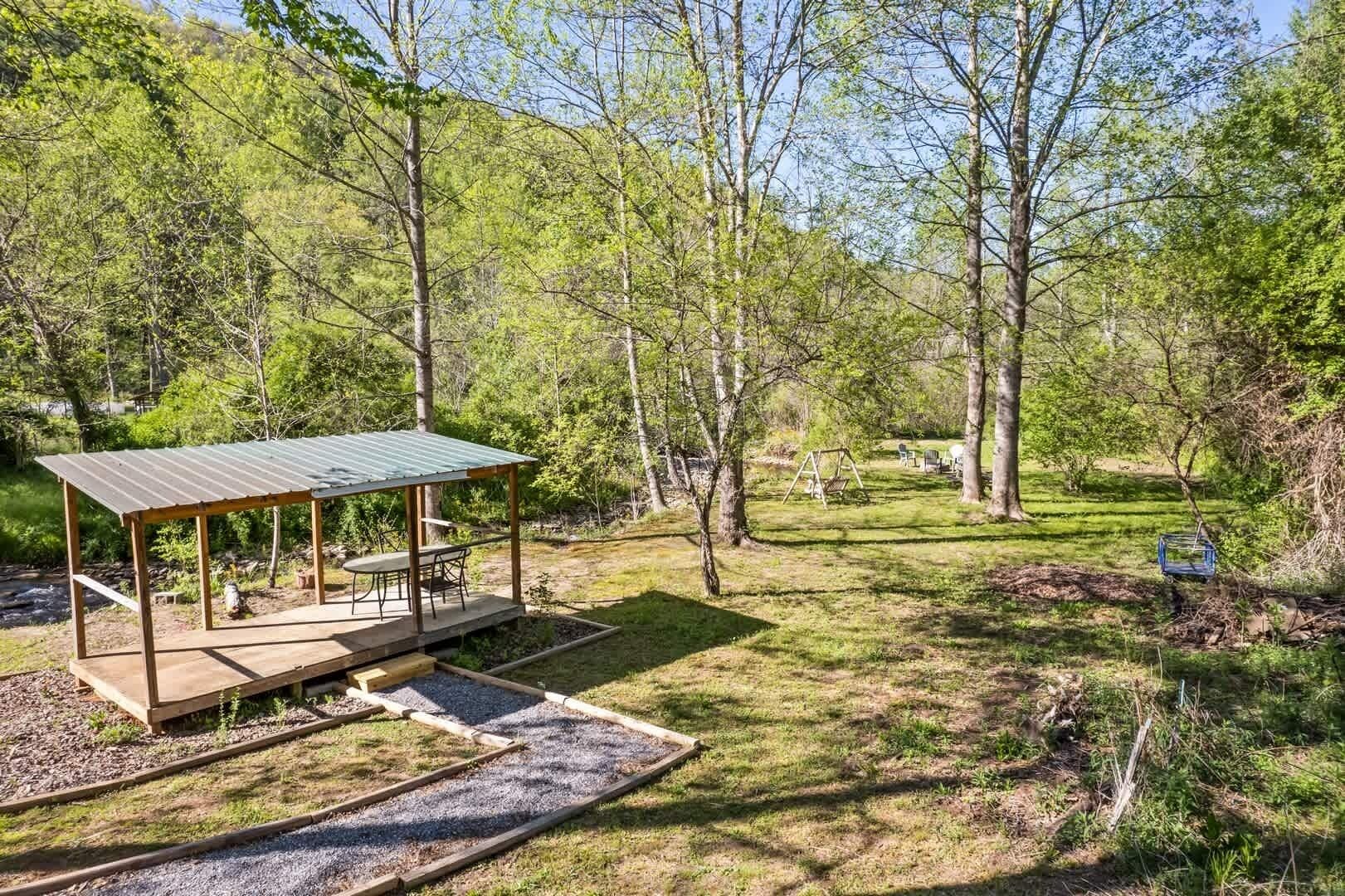 Een overdekt terras met een tafel en stoelen, omgeven door een bosrijk landschap.
