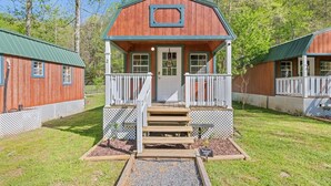 A rustic cabin with a porch, wooden steps, and a small garden area. - Treehugger Tiny Home Cabin by River Near WCU (Cullowhee)