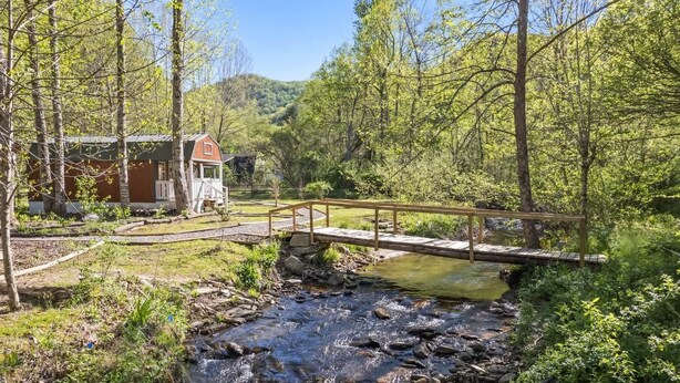 A rustic cabin with a wooden deck and a small bridge over a stream. - Treehugger Tiny Home Cabin by River Near WCU (Cullowhee)