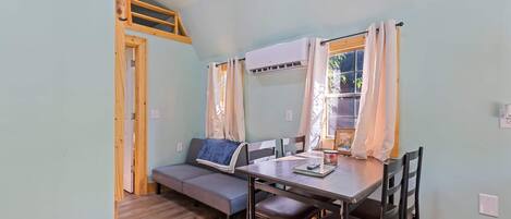 Une pièce comprenant un lit en mezzanine, un canapé, une table à manger avec des chaises et une fenêtre avec des rideaux.
