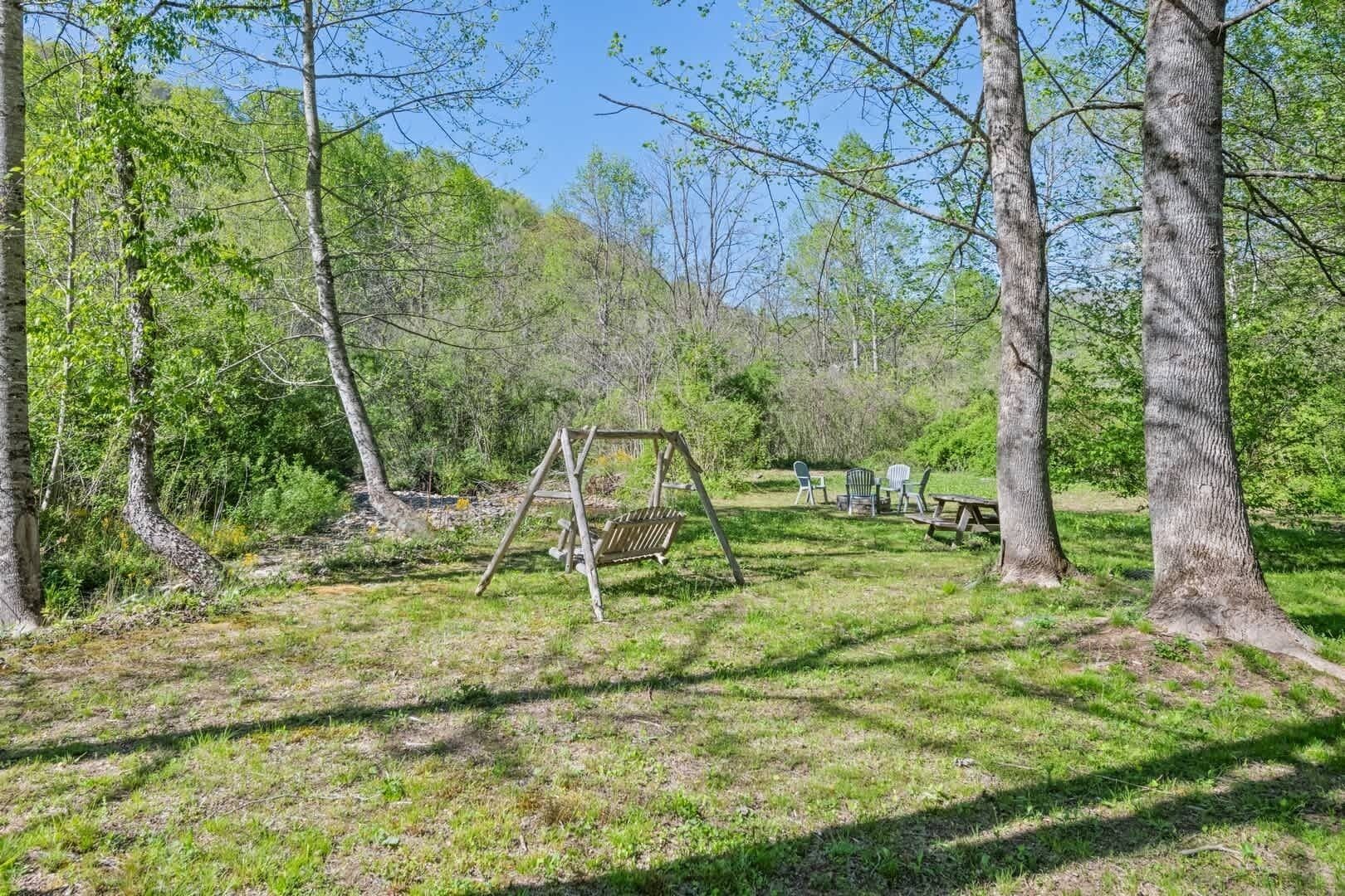 A wooded area with a swing set, picnic table, and chairs.