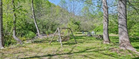 A wooded area with a swing set, picnic table, and chairs.