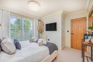 Een slaapkamer met een bed, een televisie aan de muur, een houten deur en een kleine tafel met een koffiezetapparaat.