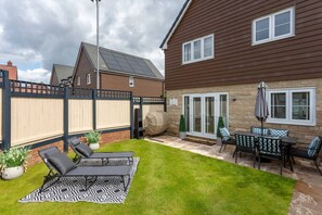 Een achtertuin met een terras, een barbecue en een zithoek met een tafel en stoelen.