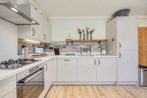 Eine moderne Küche mit wei ßen Schränken, einem Gasherd, einem Backofen, einer Holz Arbeitsplatte und einer Spritzschutzwand mit einer Mischung aus Fliesen.