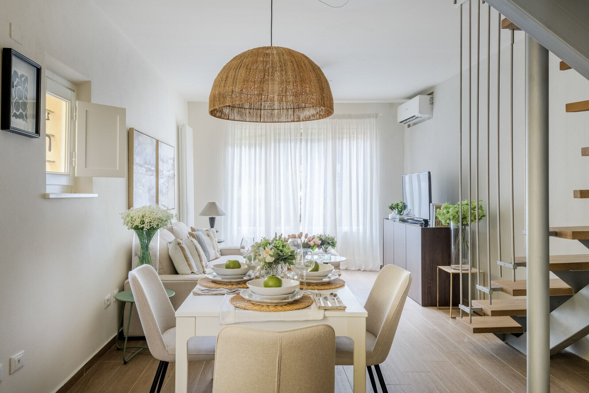 Un'area pranzo con un tavolo apparecchiato per quattro persone, un lampadario e una scala.