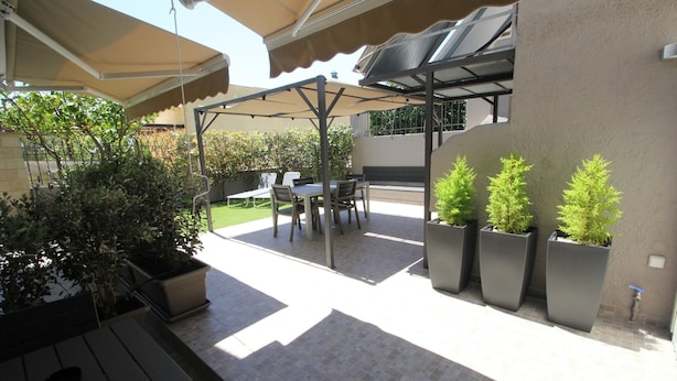 Un espace extérieur aménagé en terrasse, doté d’un coin salon couvert, de plantes en pot et offrant une vue sur la verdure environnante.
