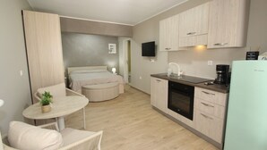 Une chambre d’hôtel compacte comprenant un coin cuisine, un espace repas avec une table et des chaises, un lit et un téléviseur fixé au mur.