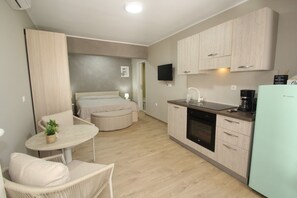 Ein kompaktes Hotelzimmer mit einer Küchenzeile, einer Essecke mit Tisch und Stühlen, einem Bett und einem an der Wand befestigten Fernseher.