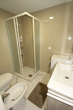 Ein Badezimmer mit Duschkabine, Waschbecken, Bidet und Waschmaschine.