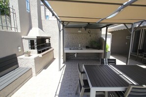 Ein Terrassenbereich im Freien mit Grill, Tisch und Bank.