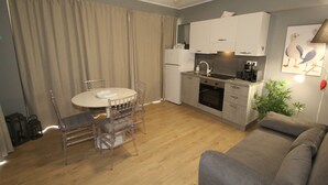 Un espacio habitable compacto con kitchenette, zona de comedor con mesa y sillas, sofá y una maceta.