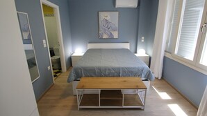 Un dormitorio con cama, mesitas de noche, un banco, un cuadro y una ventana.