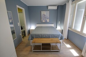 Ein Schlafzimmer mit einem Bett, Nachttischen, einer Bank, einem Gemälde und einem Fenster.
