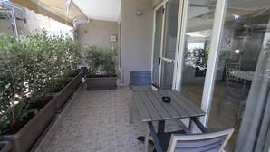 Un patio con mesa y sillas, plantas en macetas y un ventanal corredera que da a un balcón.