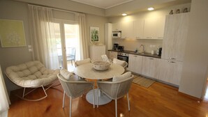 A modern kitchen with white cabinets, a round dining table with four chairs, and a rocking chair. - Dafne by Frangki (Aegina)