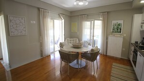 A dining area with a round table, two chairs, a ceiling light, and a kitchen area with a microwave. - Dafne by Frangki (Aegina)