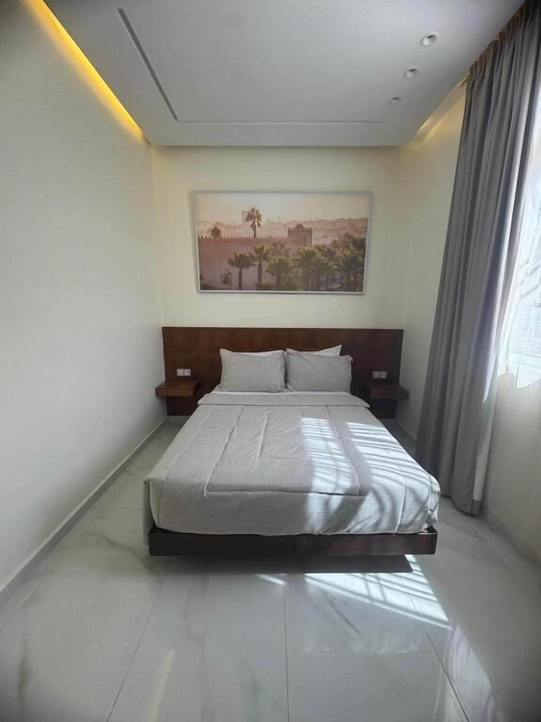 A modern hotel room with a large bed, a nightstand, a wall-mounted painting, and a window with curtains.