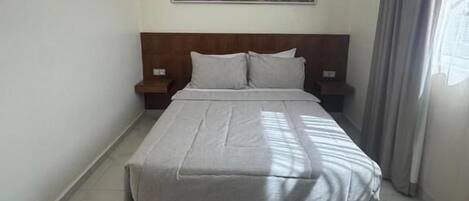 A modern hotel room with a large bed, a nightstand, a wall-mounted painting, and a window with curtains.