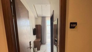 A hotel hallway with a wooden door, a number sign, and a view into a room with a bed and a window. - Hôtel Majestic (Rabat)