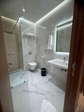 Un baño moderno con ducha envuelta en vidrio, inodoro, lavabo y espejo.
