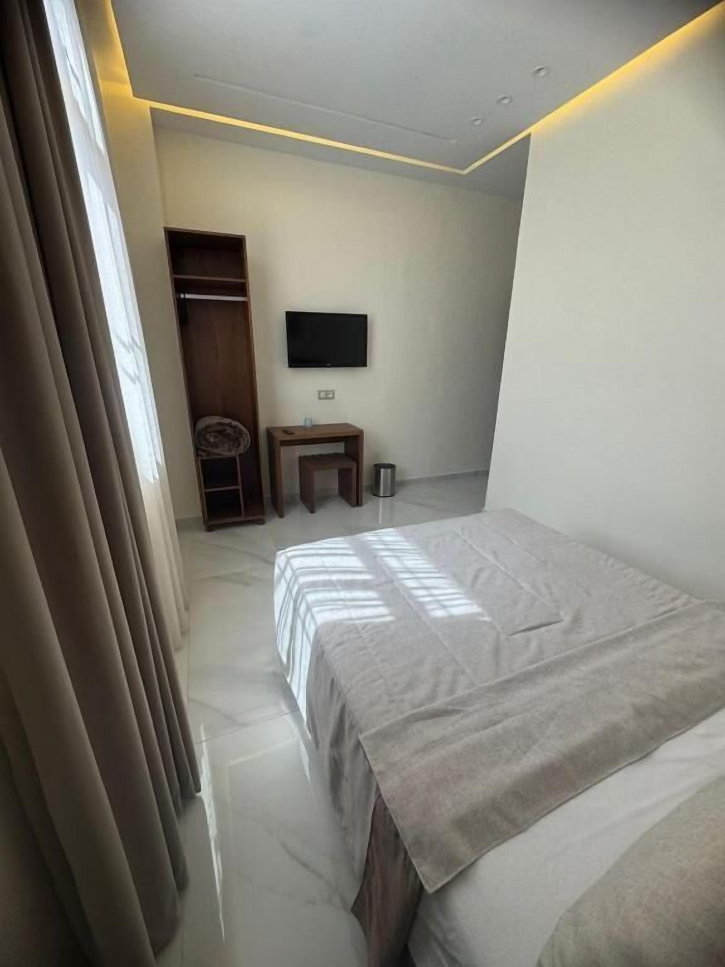 Un dormitorio con una cama, un televisor montado en la pared, una mesita y un armario.