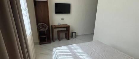 Un dormitorio con una cama, un televisor montado en la pared, una mesita y un armario.