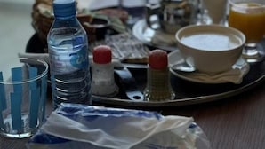 Una bandeja con productos de desayuno, incluyendo un tazón de cereal, un vaso de jugo de naranja, una botella de agua y salsas.