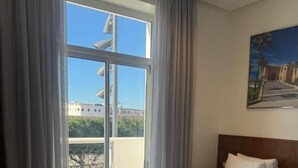 Habitación de hotel con dos camas, un ventanal con cortinas y una pintura en la pared, con vistas al exterior.