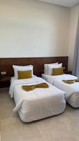 Una habitación de hotel con dos camas, cada una con ropa blanca y una almohada color mostaza.