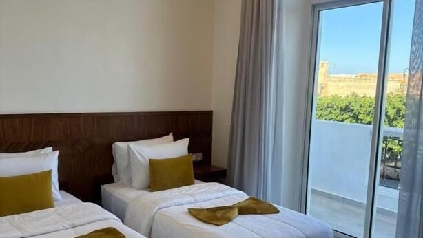 A hotel room with two beds, a large window, and a view of the outdoors. - Hôtel Majestic (Rabat)
