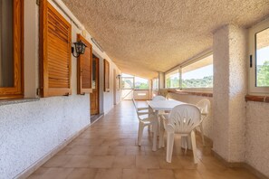 A corridor with wooden shutters, a white table with chairs, and a view through large windows. - Casa Vacanza Iris surrounded by Sulcis nature (Perdaxius)