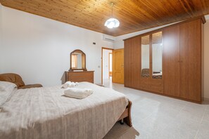 A bedroom with a bed, wooden wardrobe, and a mirror. - Casa Vacanza Iris surrounded by Sulcis nature (Perdaxius)