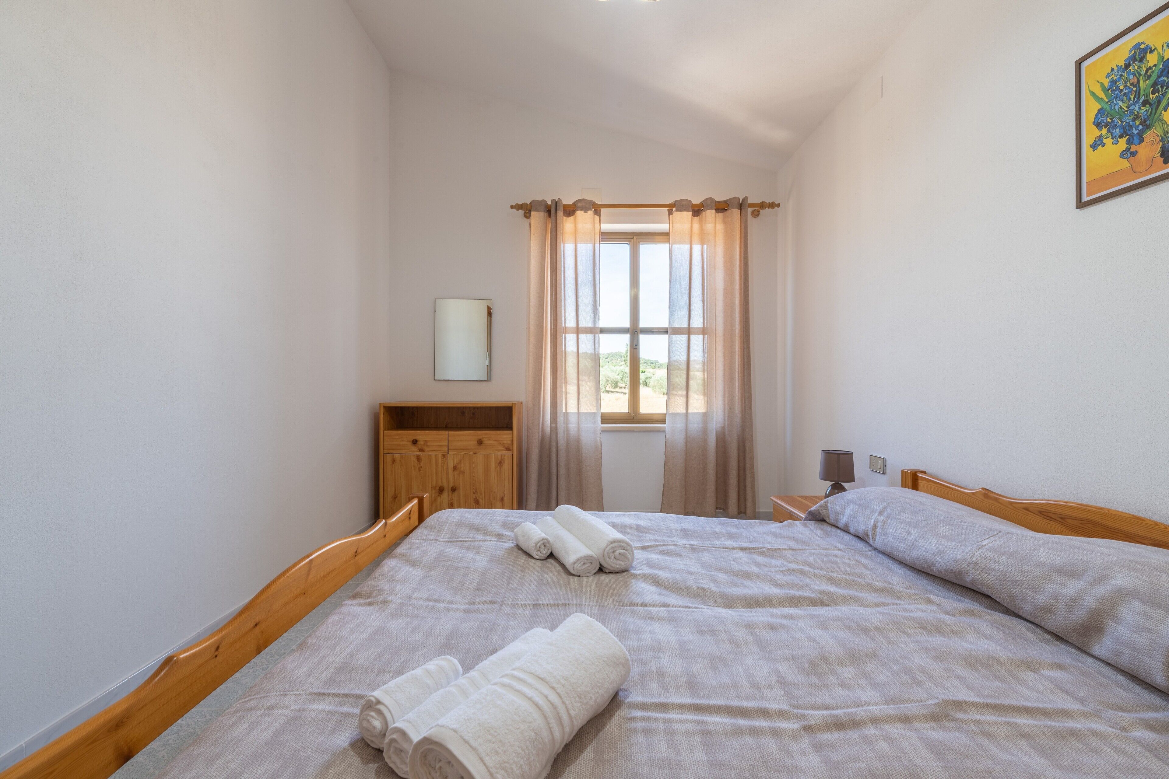 Um quarto com uma cama de madeira, um guarda-roupa de madeira, uma janela com cortinas e um quadro na parede.