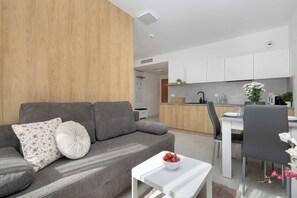 Ein modernes Wohnzimmer mit grauem Sofa, weißem Tisch und einer K üche im Hintergrund.