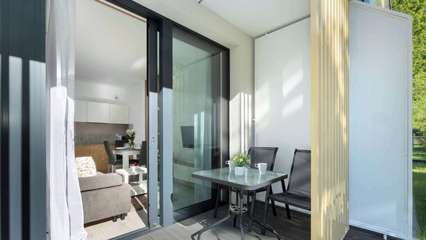 A modern outdoor patio with a glass door leading to a kitchen area, a dining table with chairs, and a sofa. - Air Conditioned Apartment | Pool | Terrace | Parking (Mielno)