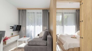 A modern room with a sofa, a small table, a bed with a wooden headboard, and a TV mounted on the wall. - Air Conditioned Apartment | Pool | Terrace | Parking (Mielno)