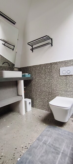 A bathroom with a white sink, mirror, towel rack, toilet, and tiled walls. - Lokal Hotels Dauin (Dauin)