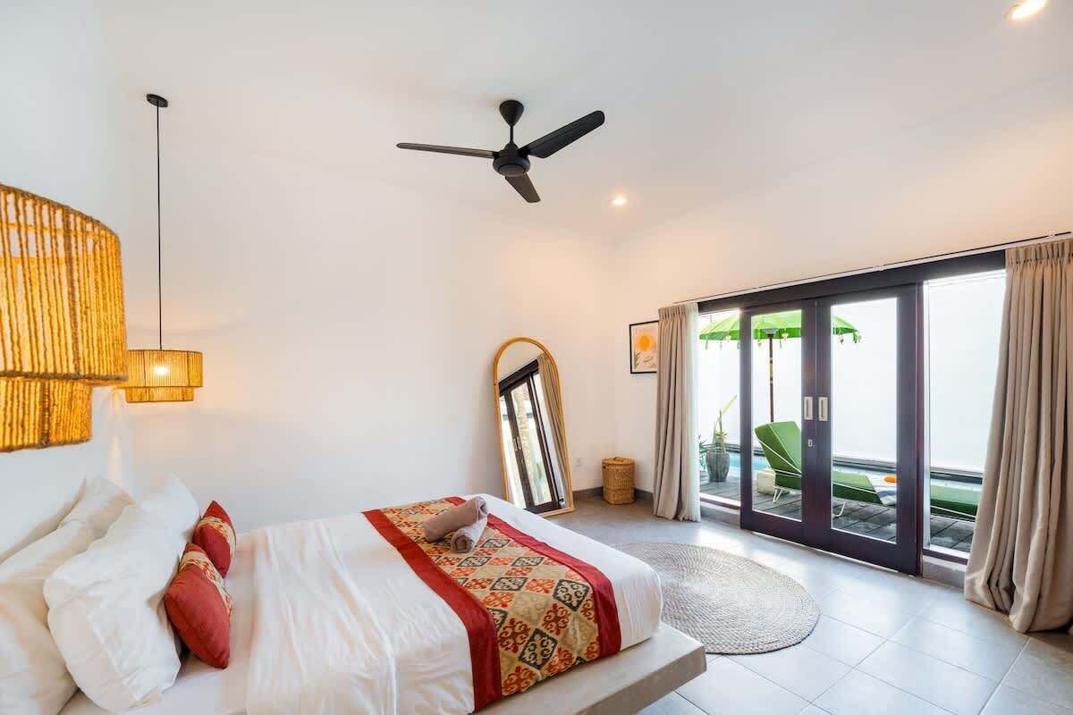 Une chambre d’hôtel avec un lit, un ventilateur de plafond, de grandes fenêtres et une vue sur l’extérieur.